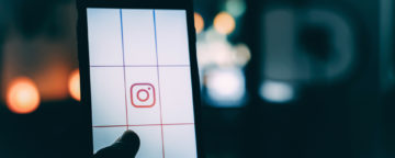 Instagram logo on phone held up against dark background. Credit: Luke van Zyl/Unsplash. Story on self-harm images on Instagram.