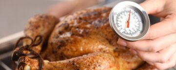 Young woman measuring temperature of whole roasted turkey with food thermometer