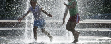 Children play outdoors in water fountain.