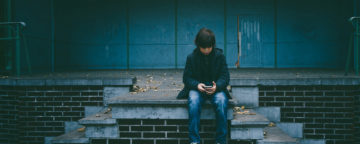 Young teenager sits alone looking down at their smartphone. Credit: Gaelle Marcel/Unsplash.