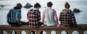 Group of teens sitting looking away from camera at the water.